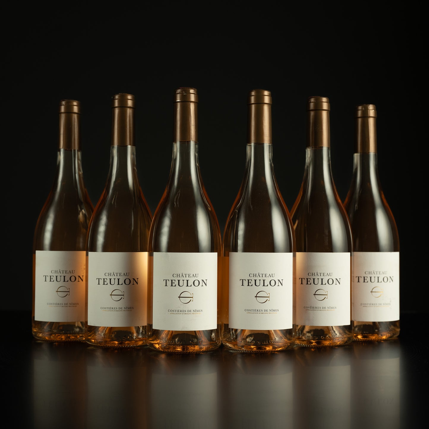 Six bottles of Chéteau Teulon wine arranged in a row on a dark background
