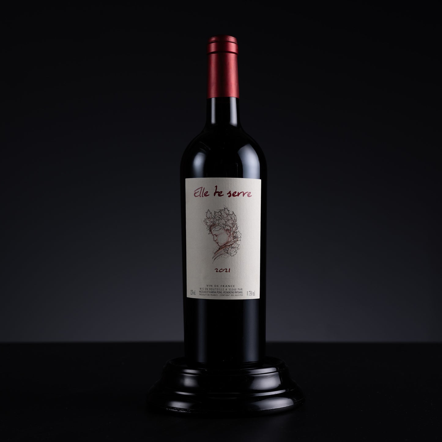 A single dark wine bottle with a cream label reading 'elle te serre' and '30%1' stands centered on a black surface against a dark gradient background.
