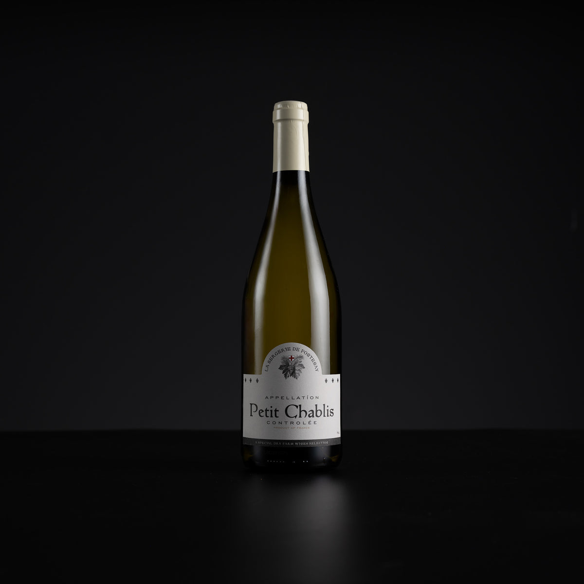 A single bottle of Petit Chablis white wine stands centered against a very dark black background, with a white label and pale foil at the neck.