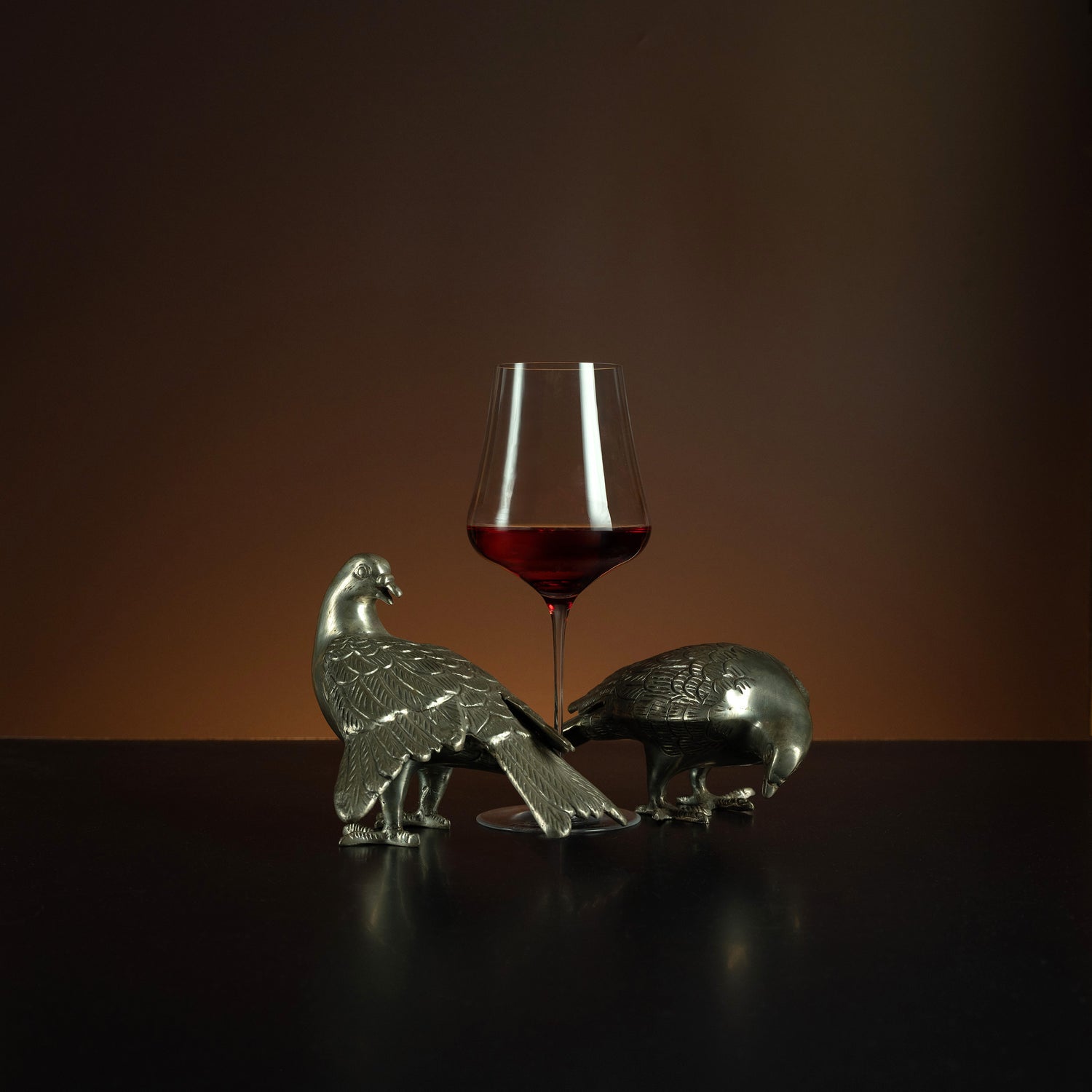 Decorative animal figures with a glass of red wine on a dark surface