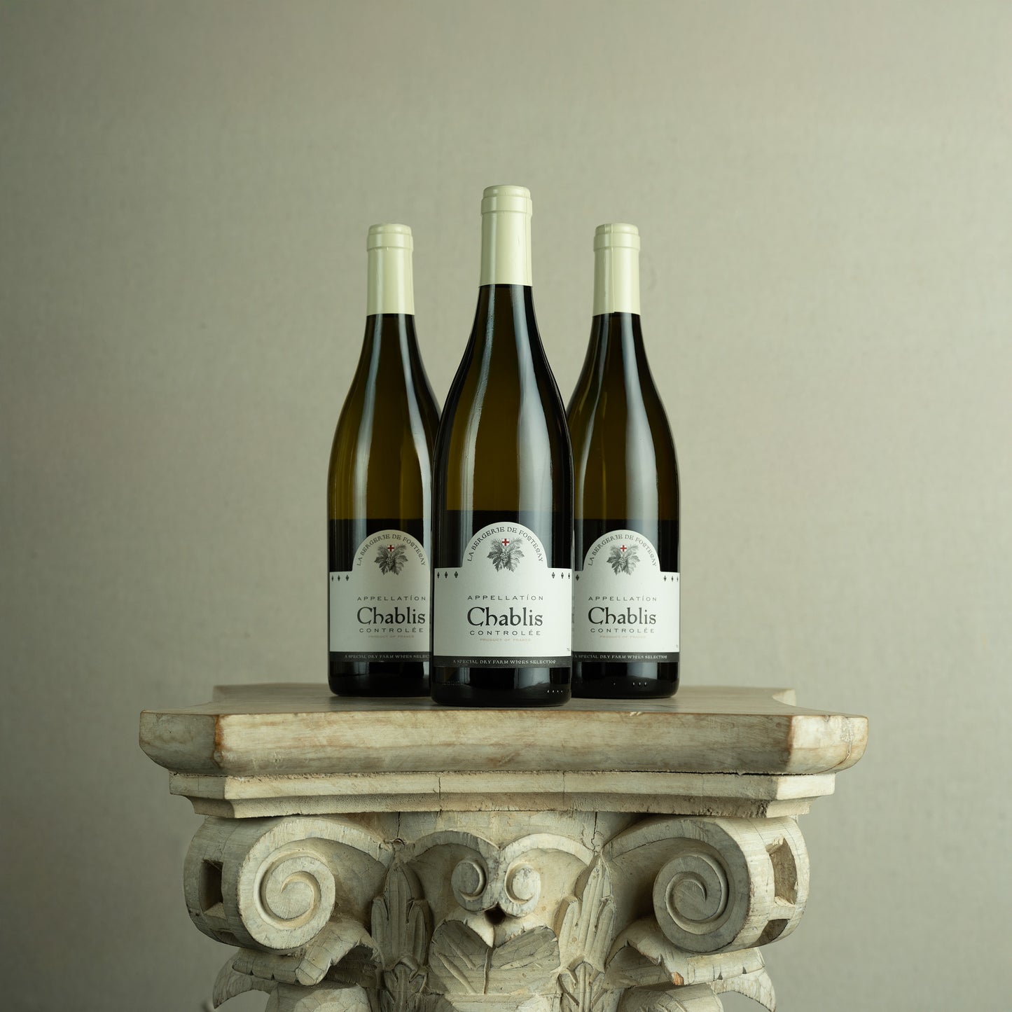 Three bottles of Chablis wine on a decorative stone pedestal against a plain background
