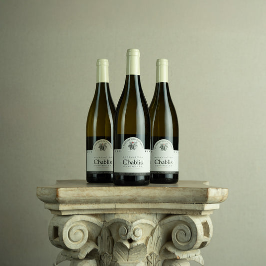 Three bottles of Chablis wine on a decorative stone pedestal against a plain background