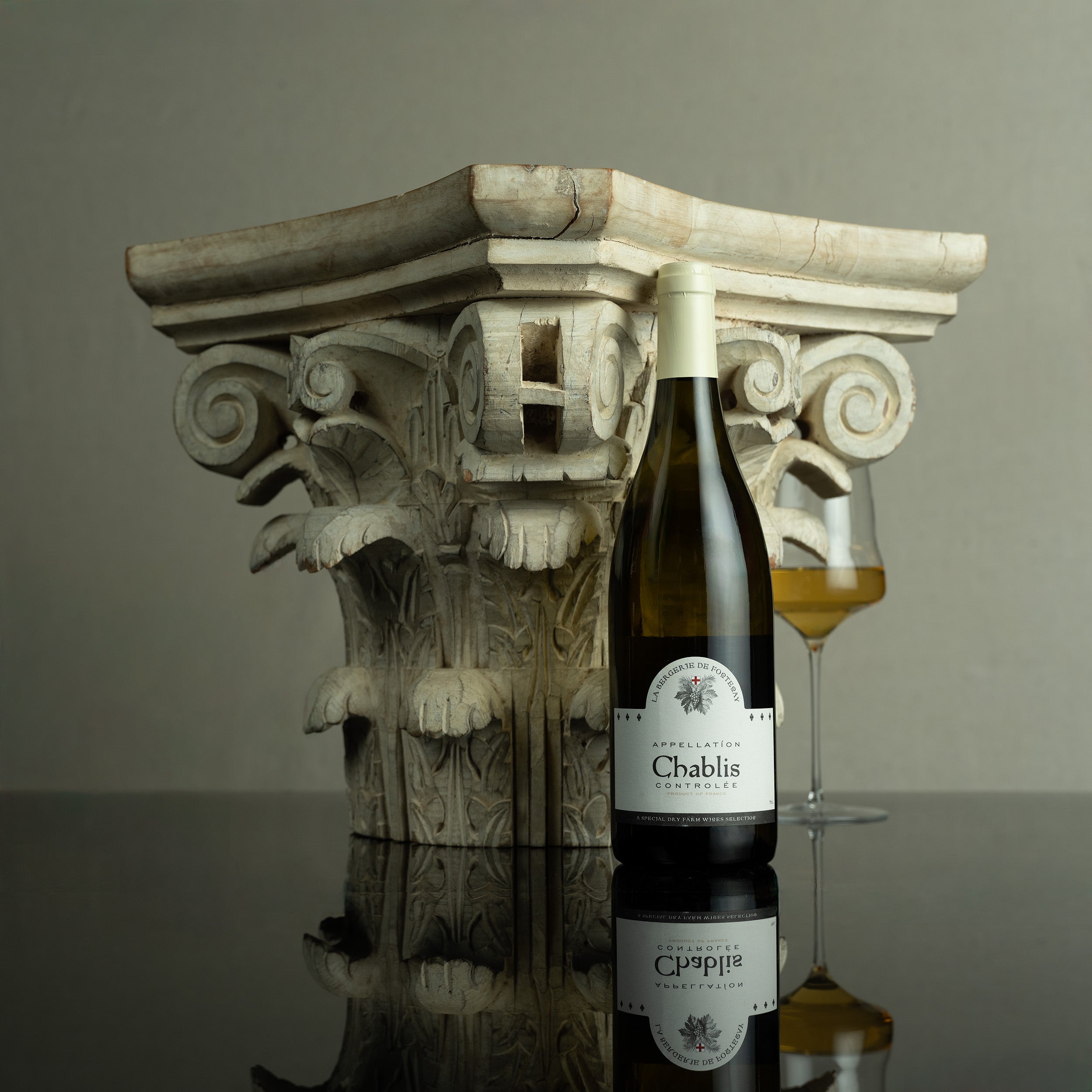 Chablis wine bottle with a glass on a decorative stone column against a gray background