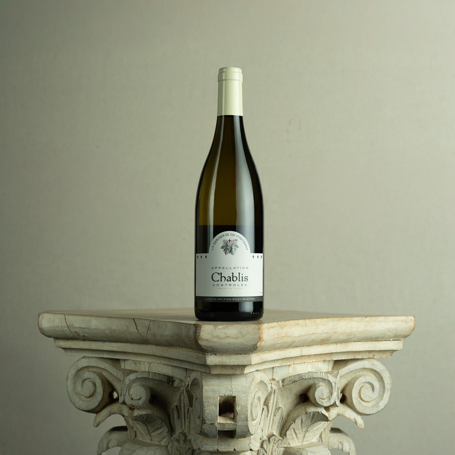 Bottle of Chablis wine on a decorative stone pedestal against a plain background