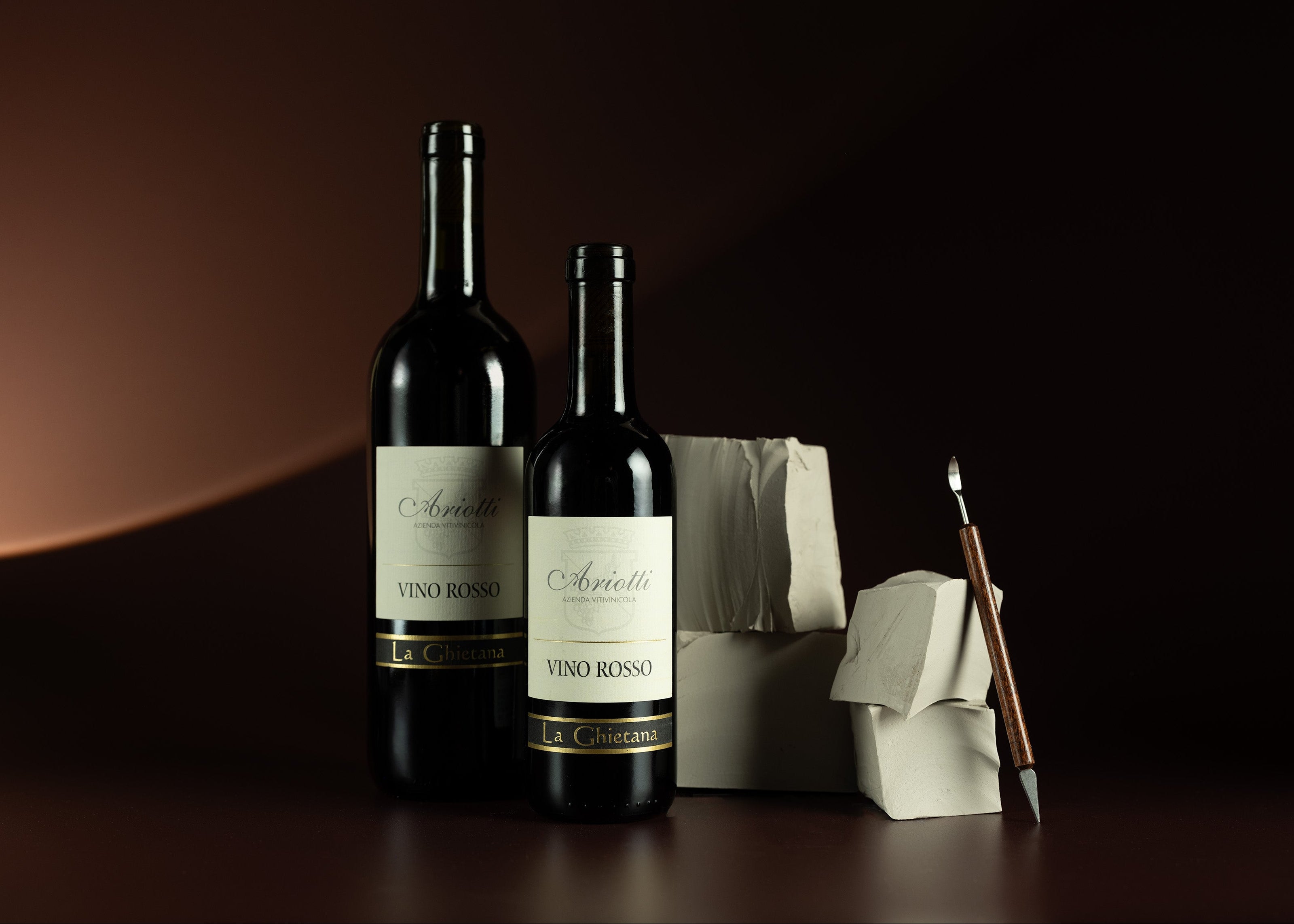 Two bottles of Vino Rosso wine on a dark surface with a brush and cloth.