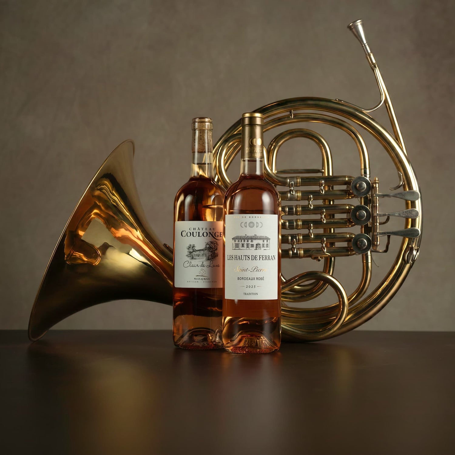 Two bottles of Cuvée de la Reine with a French horn on a dark surface.