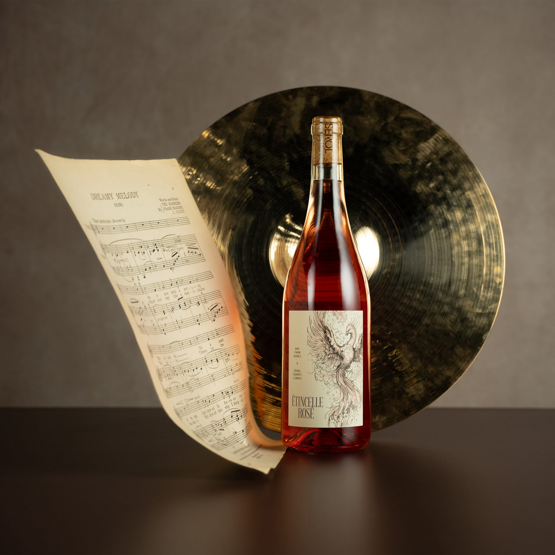 Wine bottle with a label on a dark surface with sheet music and a cymbal in the background