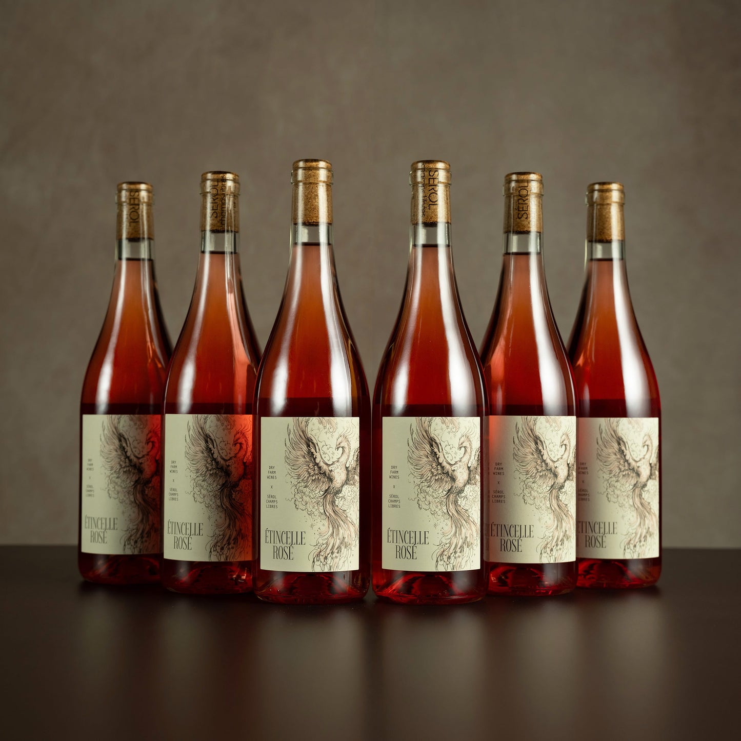 Six bottles of Domaine Rosé wine on a dark surface with a neutral background