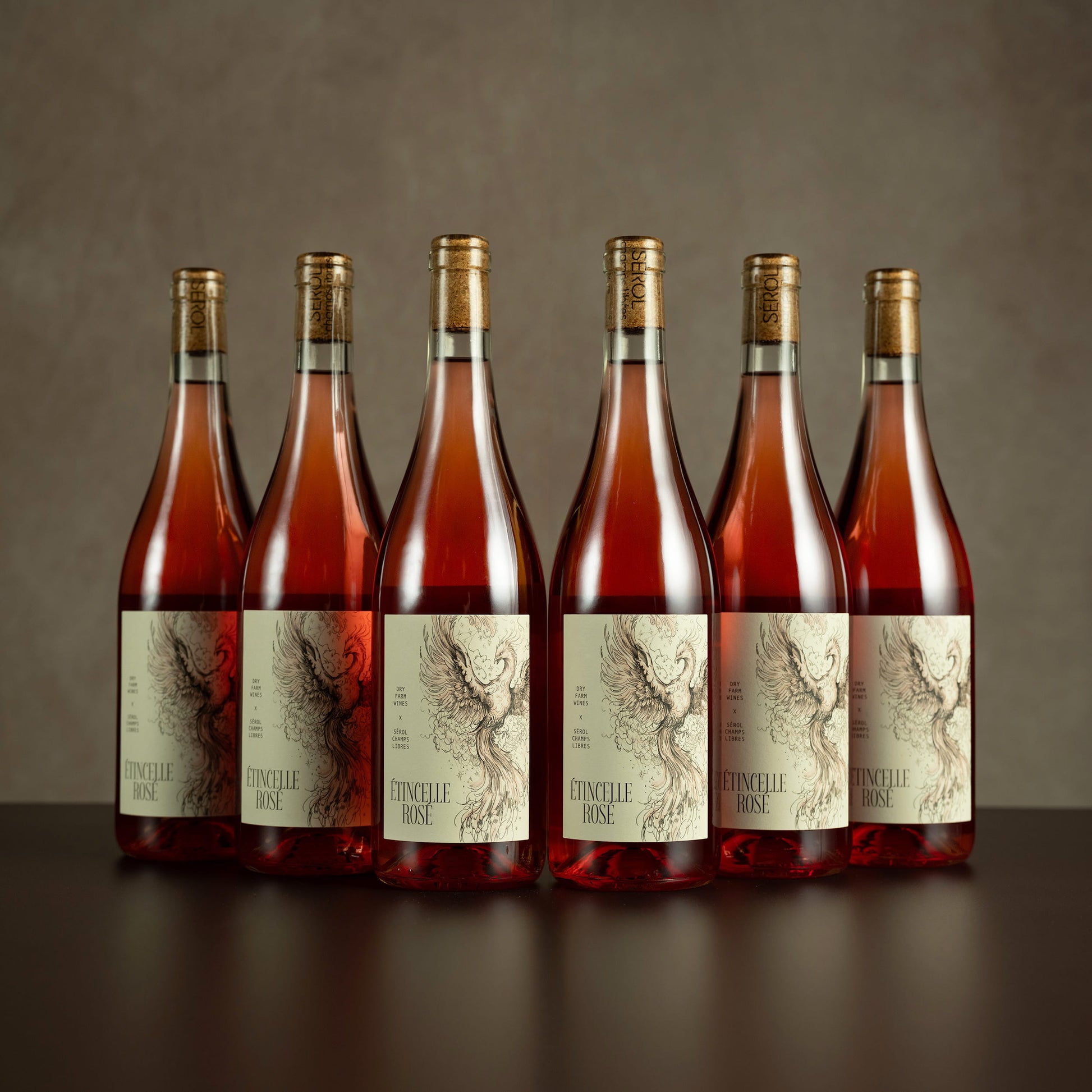 Six bottles of Domaine Rosé wine on a dark surface with a neutral background