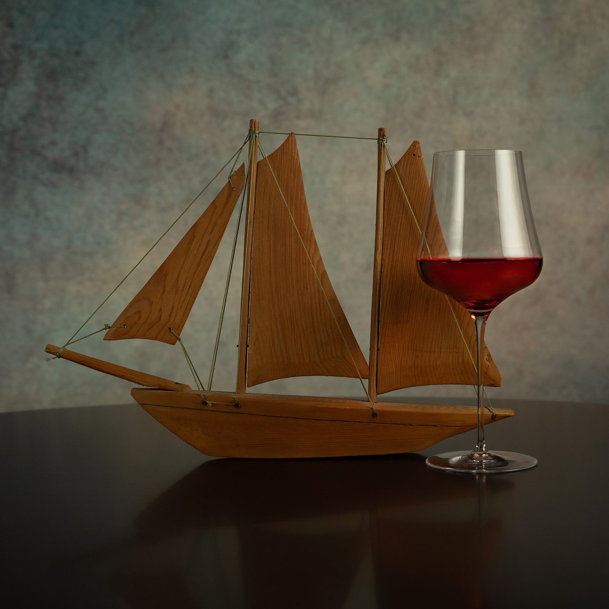 Wooden sailboat model with a glass of red wine on a reflective surface