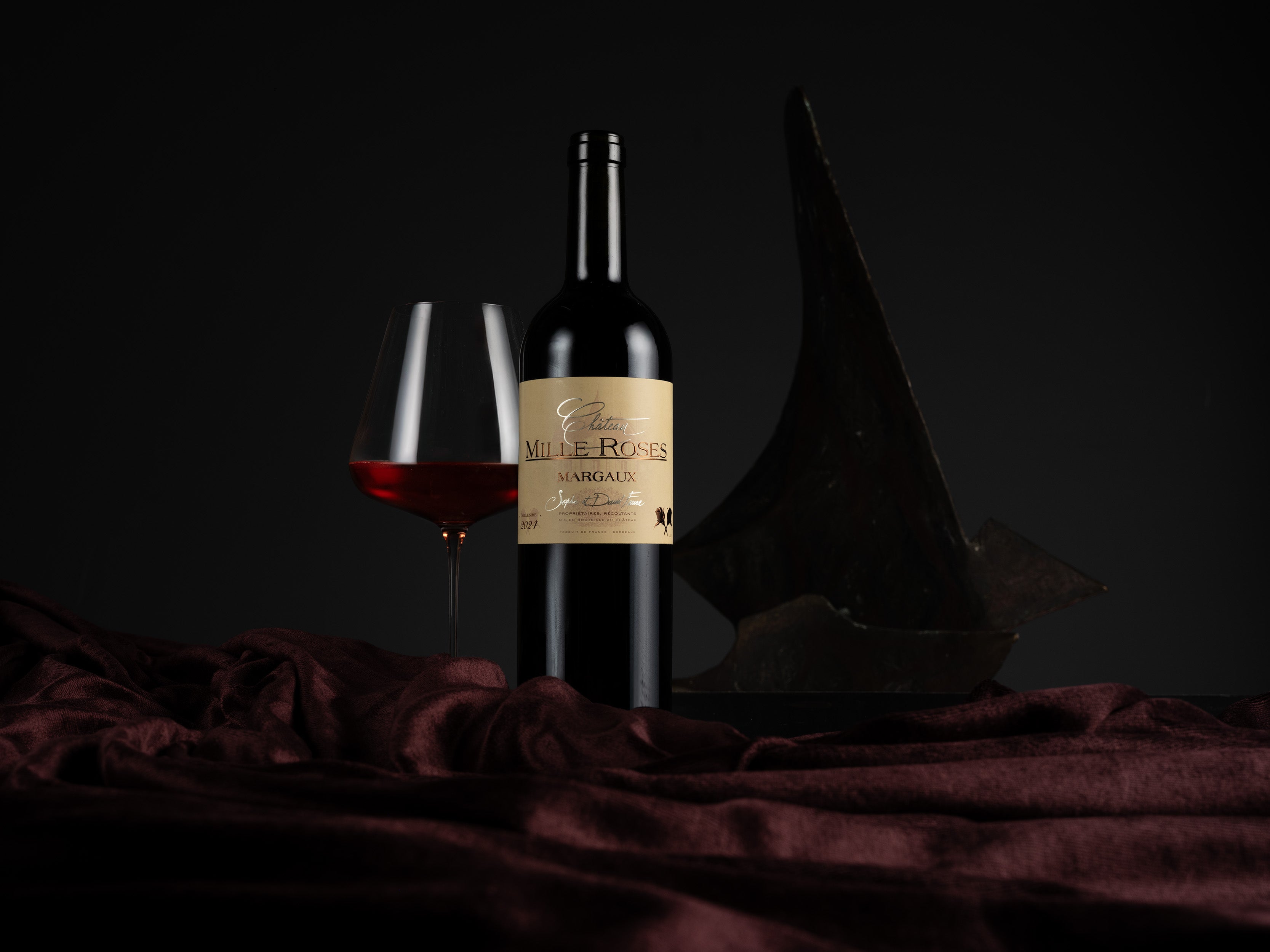 Wine bottle and glass on a dark background with a decorative hat.