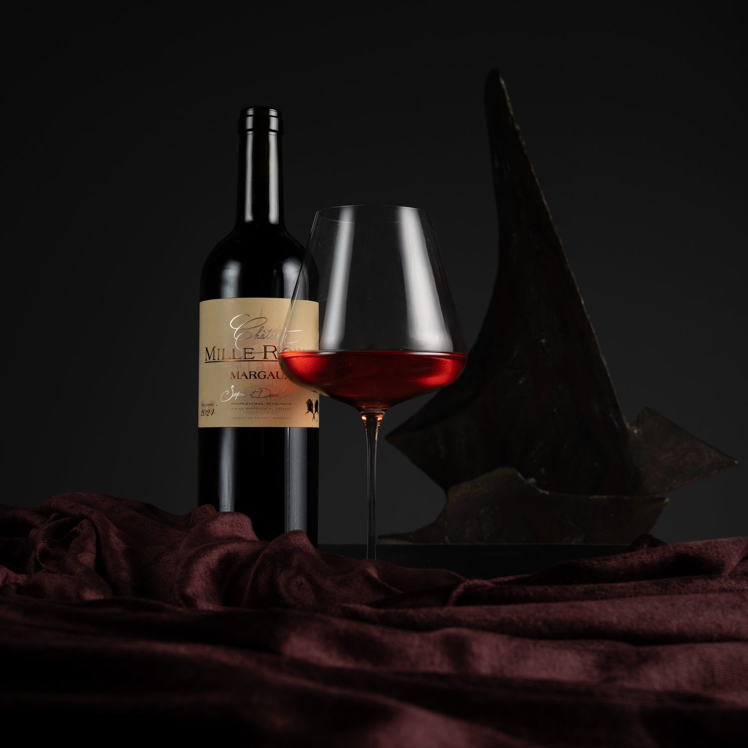 Bottle and glass of red wine with a dark background