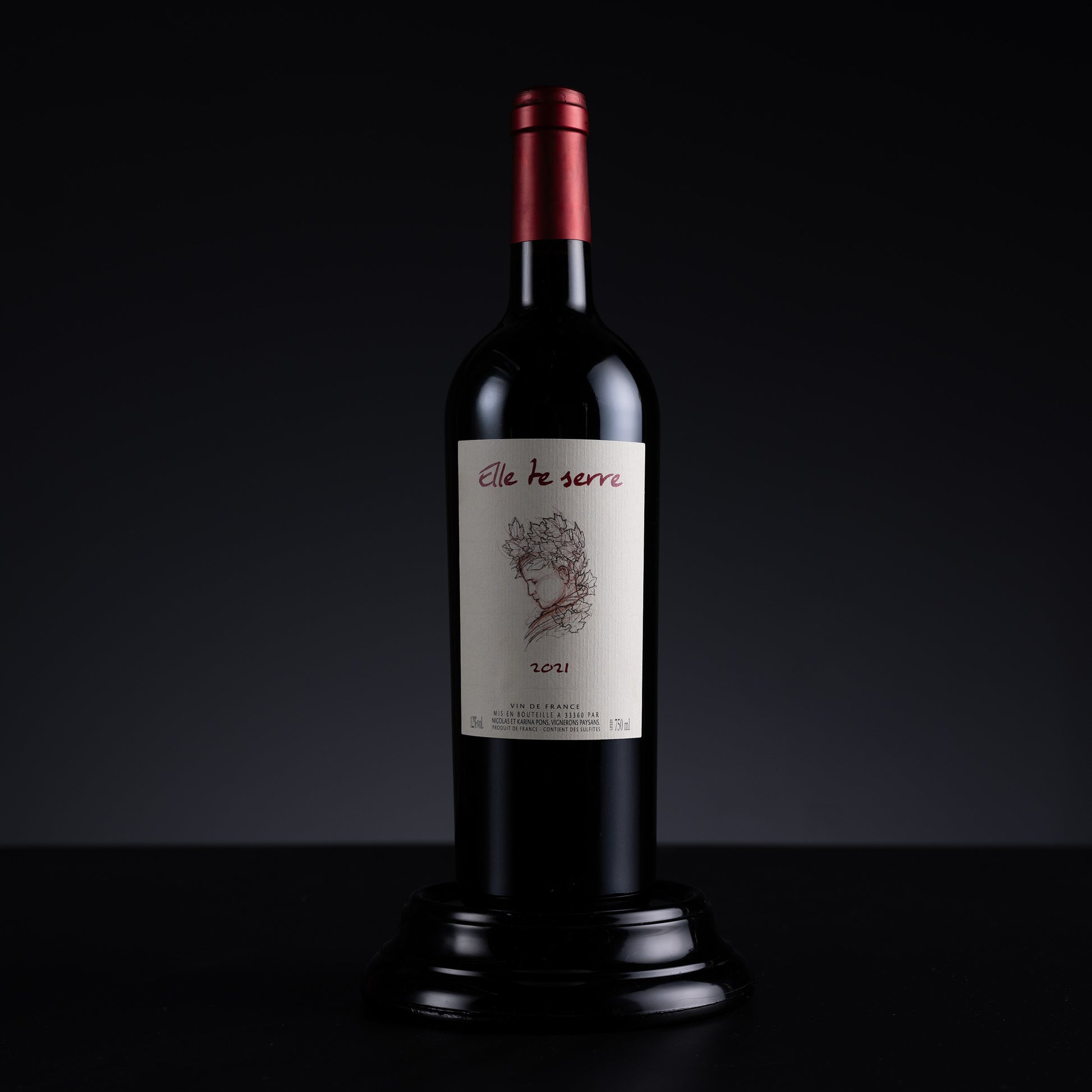 A single dark wine bottle with a cream label reading 'elle te serre' and '30%1' stands centered on a black surface against a dark gradient background.