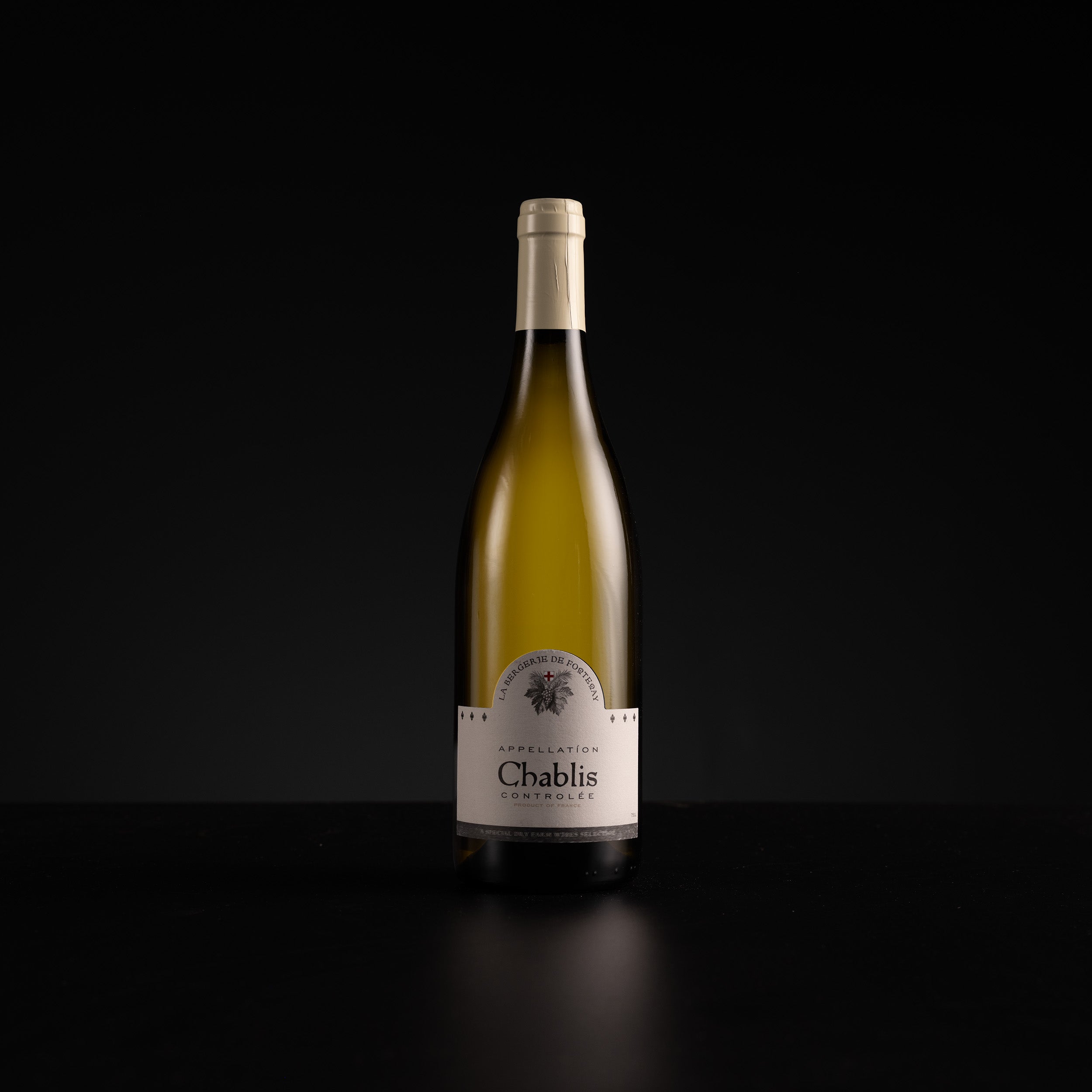 A single bottle of Chablis white wine centered against a solid black background, with a cream-colored label and foil capsule.