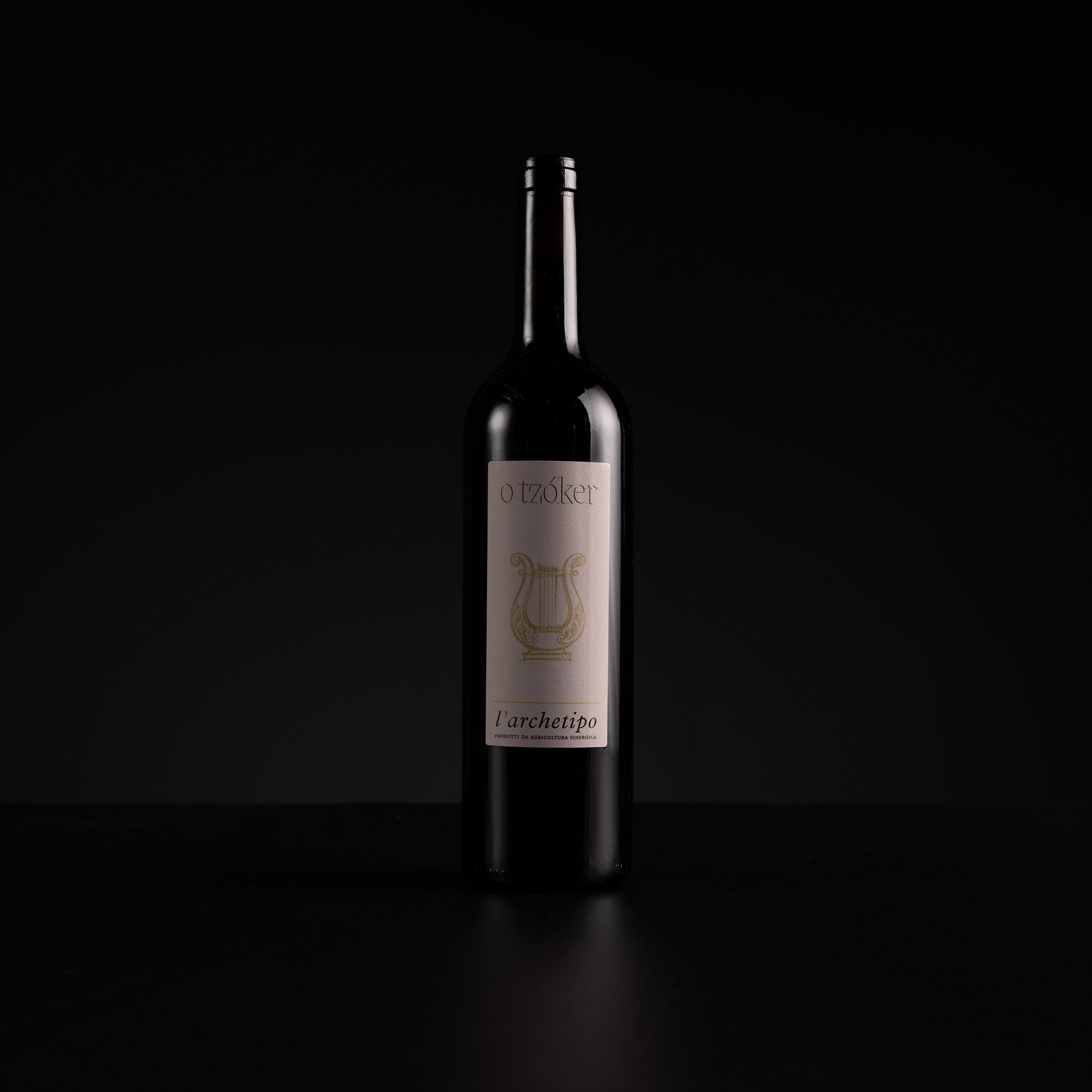 A single dark wine bottle with a cream label and gold lyre logo, standing on a black surface against a black background.
