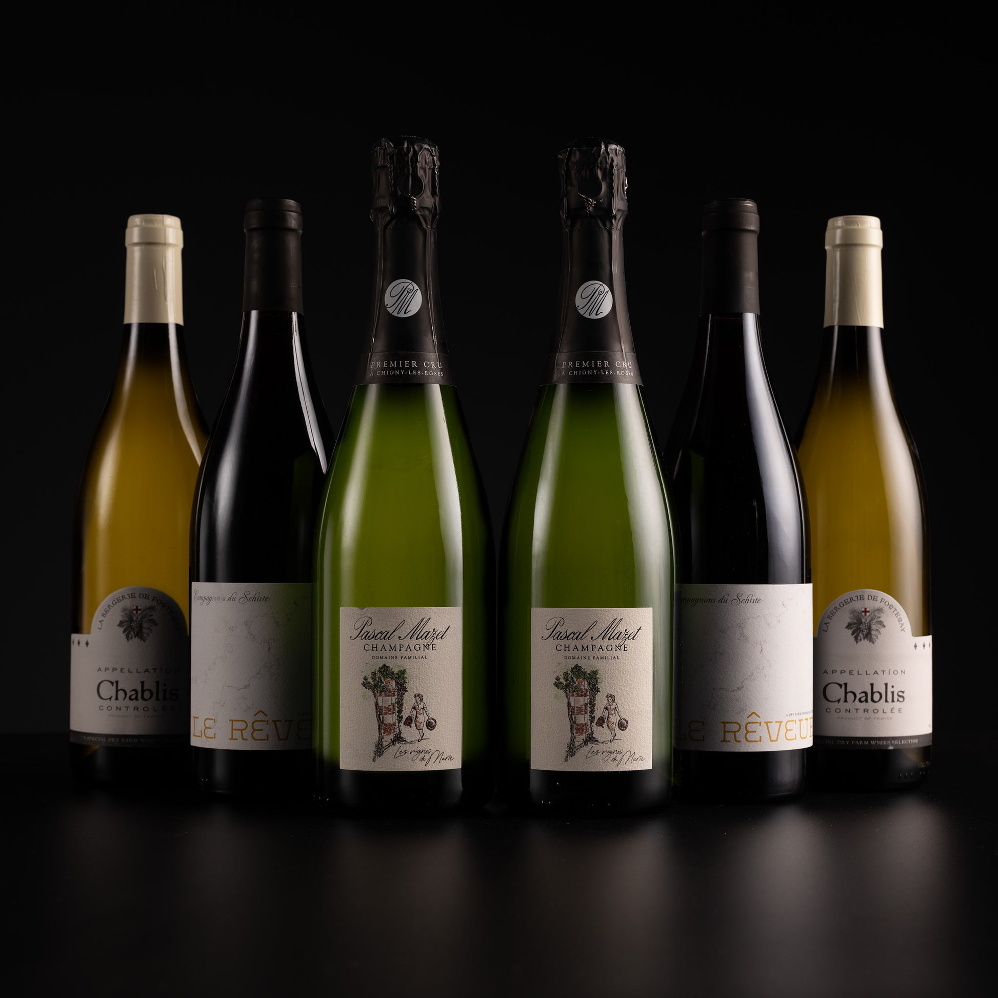 Six wine bottles arranged in a row against a black background, including Chablis and sparkling wine bottles with cream, black, and green labels.