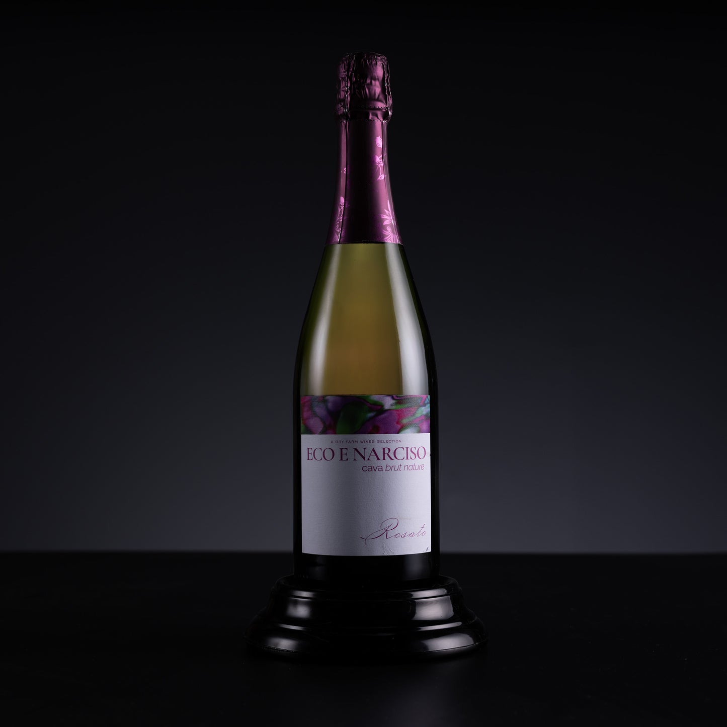 A bottle of R.O. Enarciso Gran Reserva champagne displayed on a black pedestal against a dark studio background.