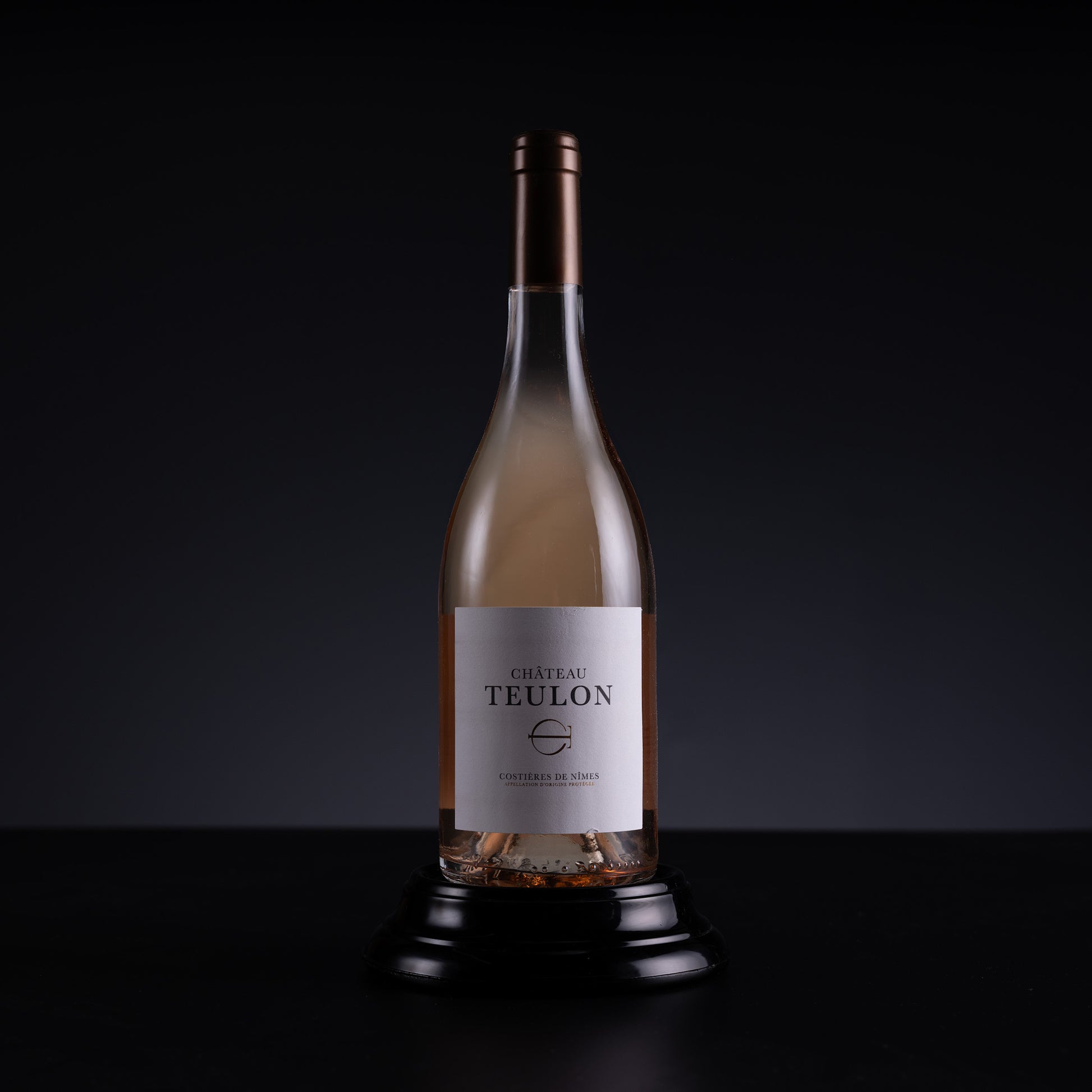 A bottle of Chateau Teulon Rosé de Vin non-alcoholic, displayed on a black stand against a dark studio background.