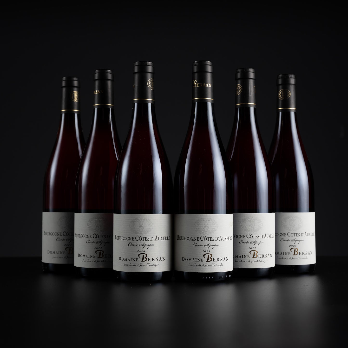 Six bottles of Domaine Bérans red wine arranged in a row against a dark studio background, with white labels and black caps.