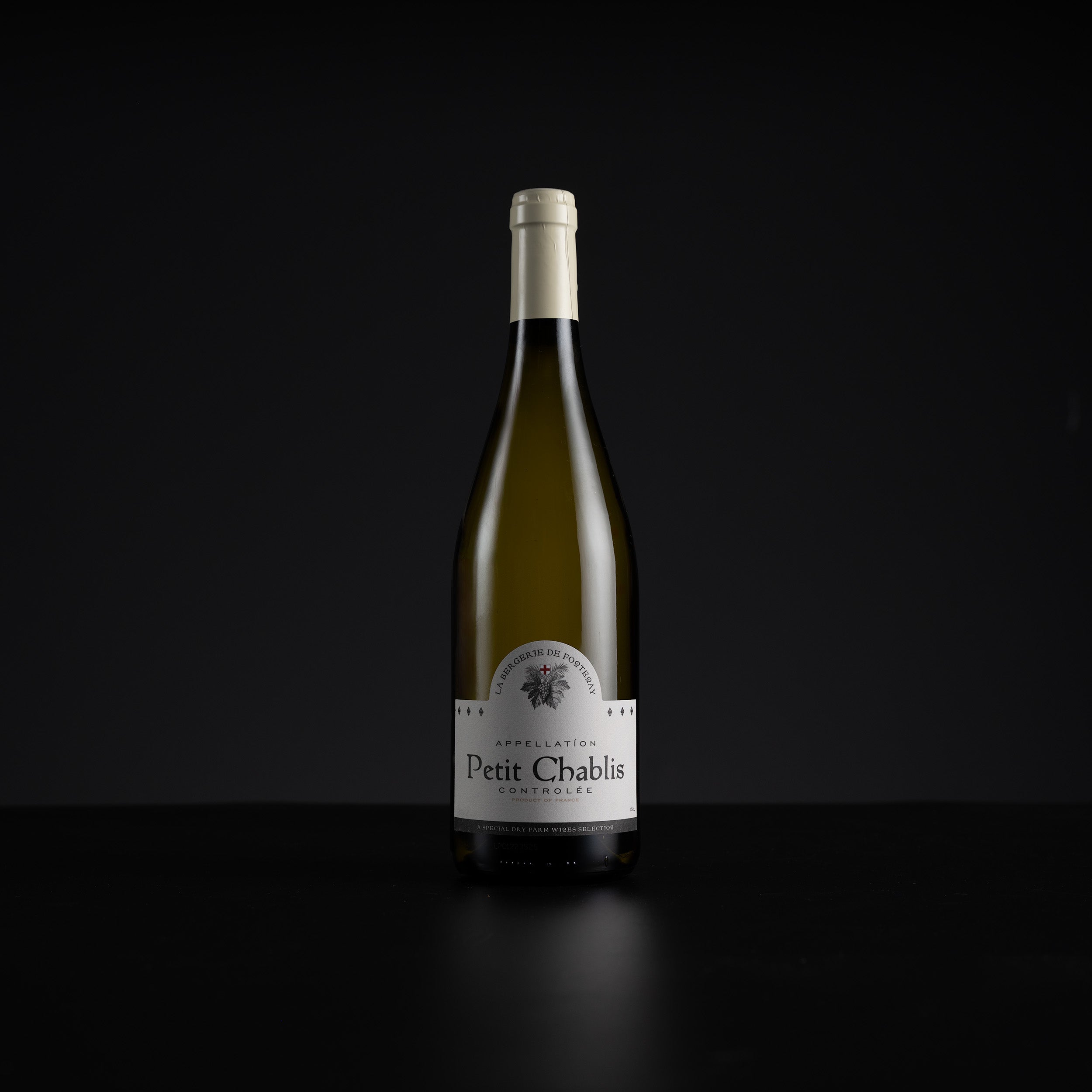 A single bottle of Petit Chablis white wine stands centered against a very dark black background, with a white label and pale foil at the neck.