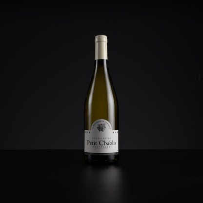 A single bottle of Petit Chablis white wine stands centered against a very dark black background, with a white label and pale foil at the neck.