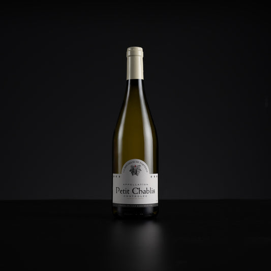 A single bottle of Petit Chablis white wine stands centered against a very dark black background, with a white label and pale foil at the neck.