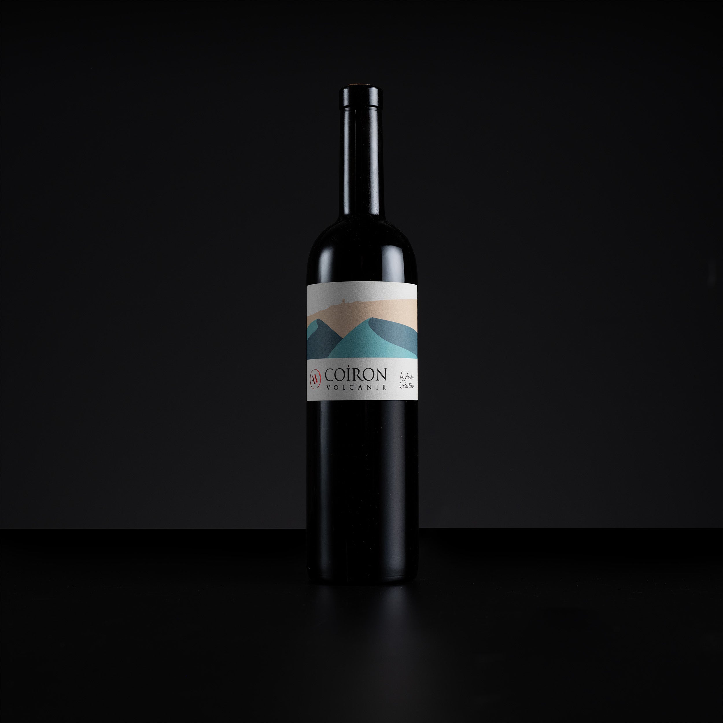 A single dark wine bottle with a minimalist label featuring a mountain design in blue, beige, and white, set against a solid black background.
