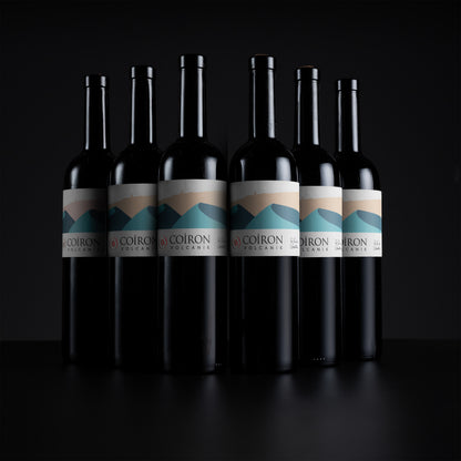 Six dark wine bottles with white labels featuring a blue and beige mountain graphic, arranged in a row against a black background. The label text reads 'COIRON OREGON'.