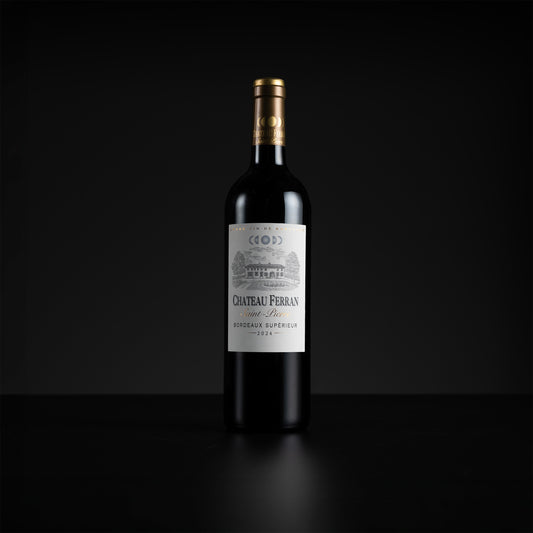 A single bottle of Chateau Ferran Saint-Beau Red (red wine) with a white label and gold foil, standing on a dark reflective surface against a black background.