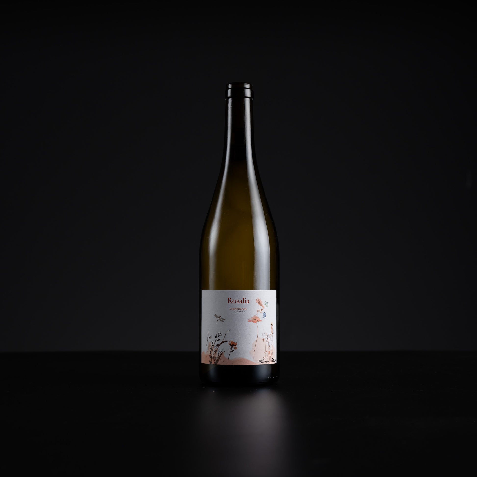A single dark glass wine bottle with a white label featuring delicate pink floral illustrations, set against a solid black background.