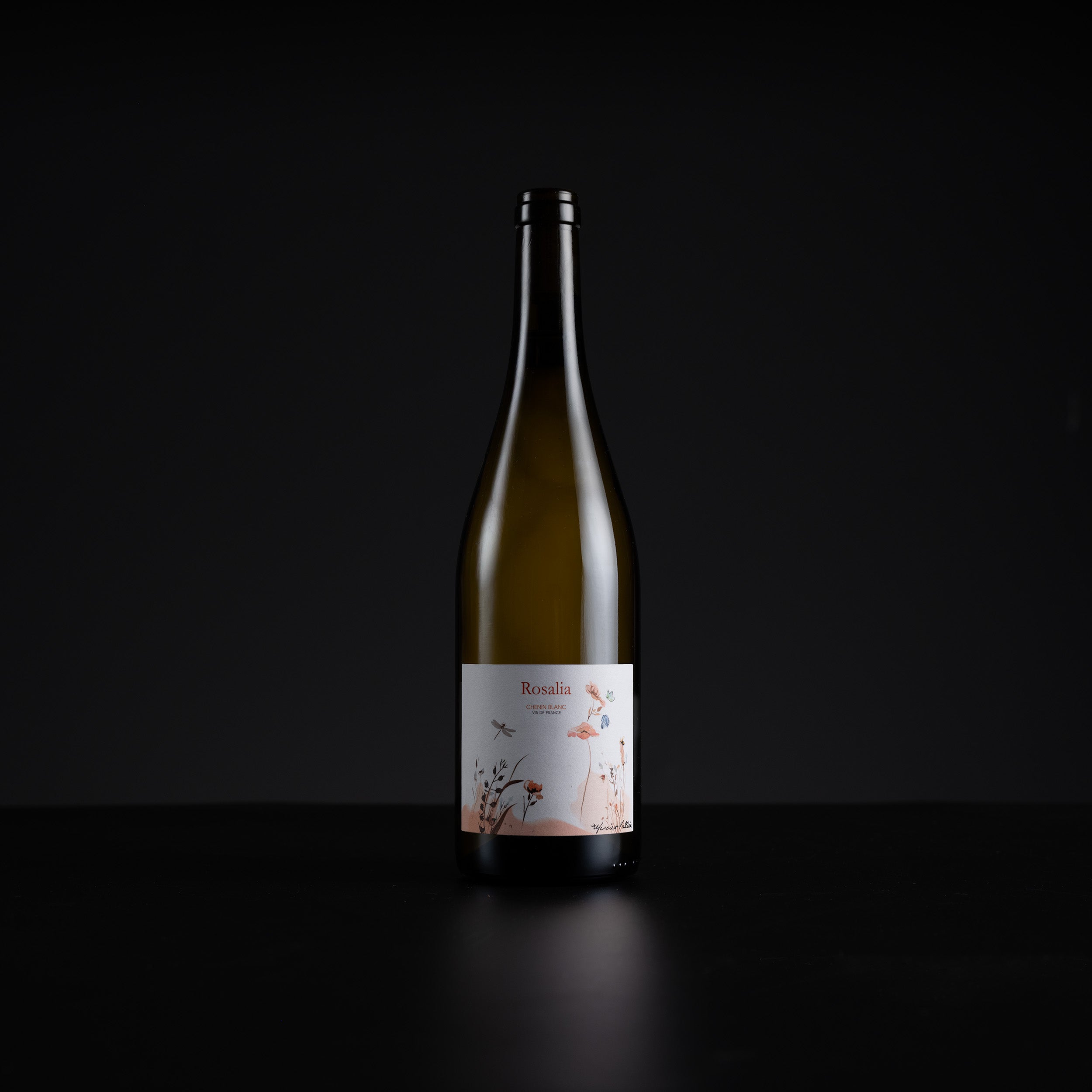A single dark glass wine bottle with a white label featuring delicate pink floral illustrations, set against a solid black background.