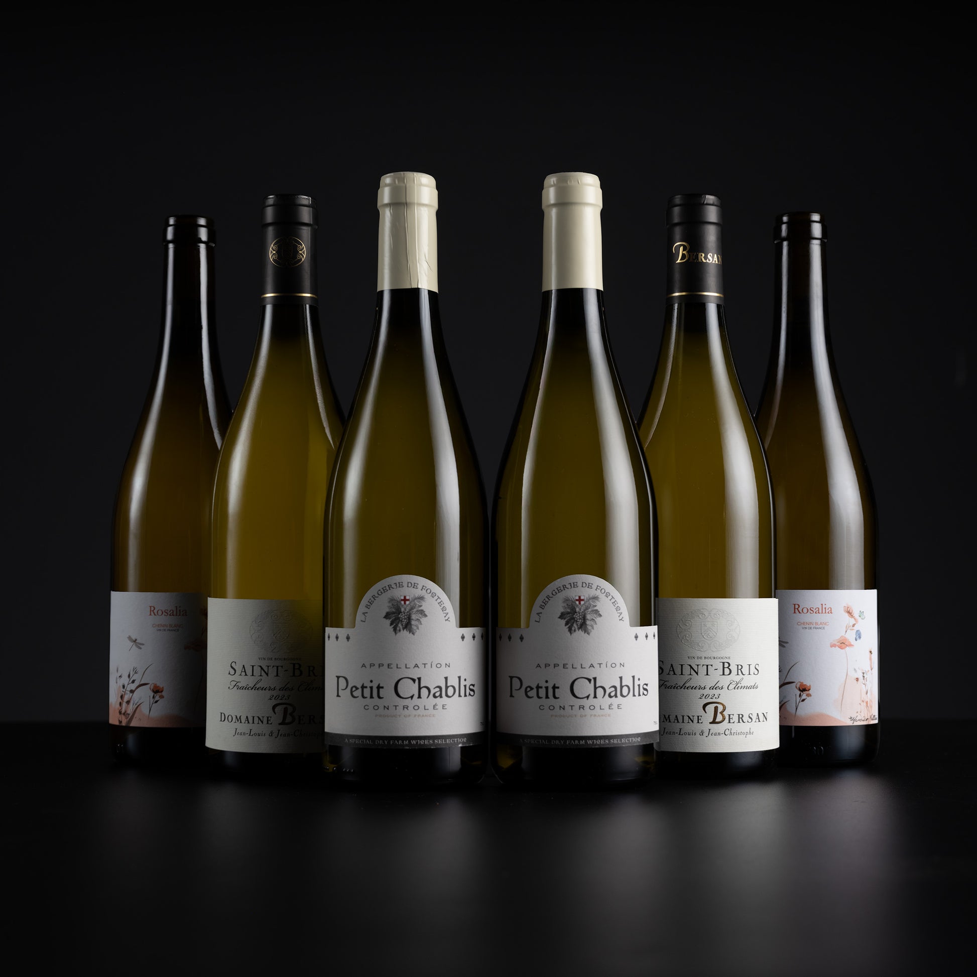 Six white wine bottles from the brand Rescadis, including Petit Chablis and Saint-Bre, arranged in a row against a dark studio background.