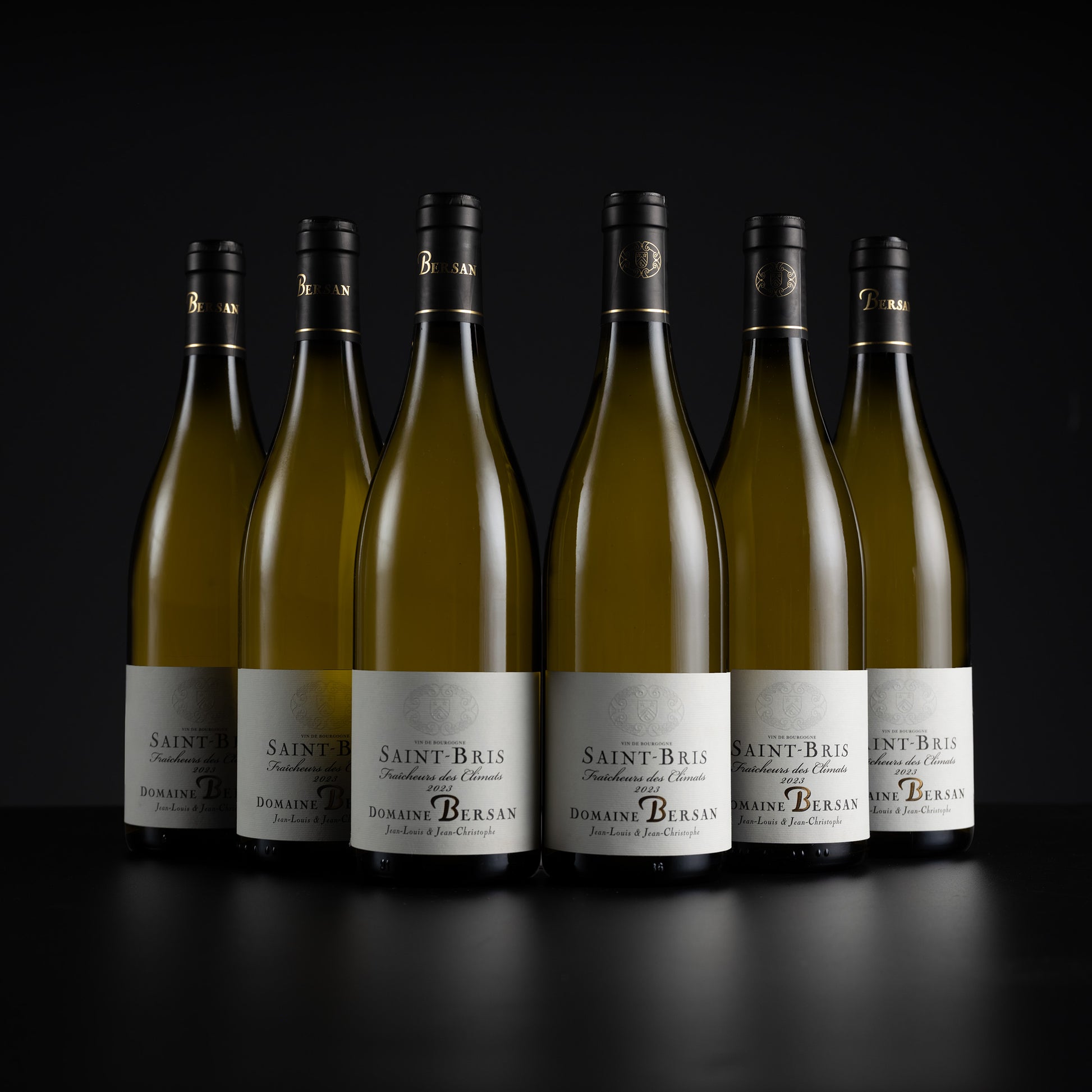 Six bottles of Domaine Berrasan Saint Bris white wine arranged in a row against a dark black background.