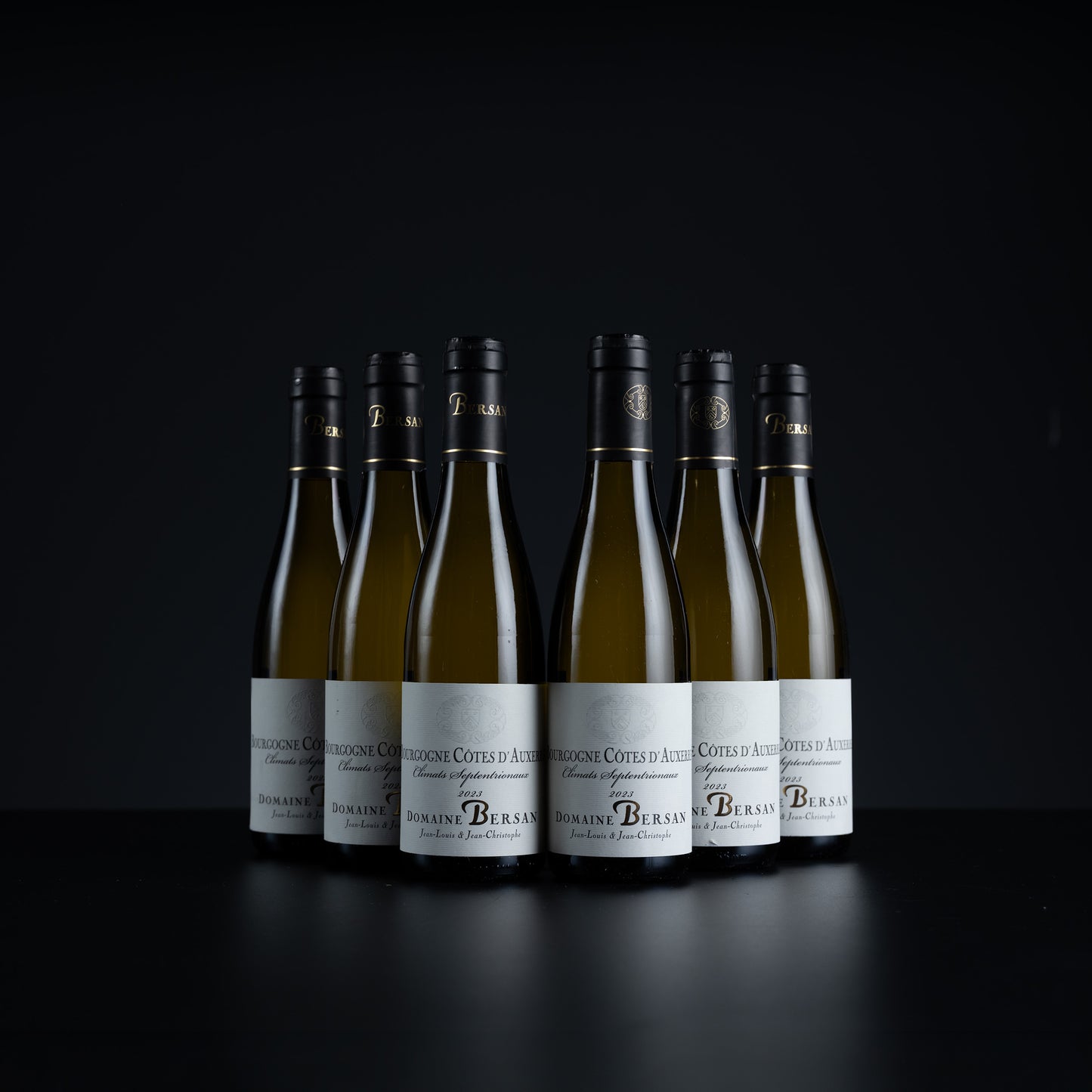 Six bottles of Dom Pérignon Grand Cru Bon Voyage white wine arranged in a row on a dark reflective surface against a black background.