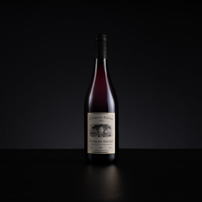 A single bottle of red wine from the brand Cotes du Rhone, specifically Florian Andre, standing upright on a dark reflective surface against a solid black background.