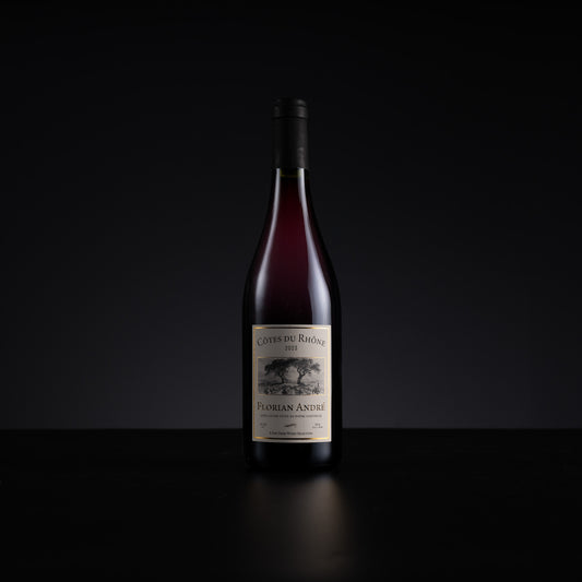 A single bottle of red wine from the brand Cotes du Rhone, specifically Florian Andre, standing upright on a dark reflective surface against a solid black background.