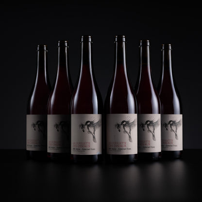 Six dark glass wine bottles with cream labels and black winged illustrations, arranged in a row against a black background. The front bottle label reads 'LA CERVELLLE LAVANDELLA' and 'RED BURGUNDY'.