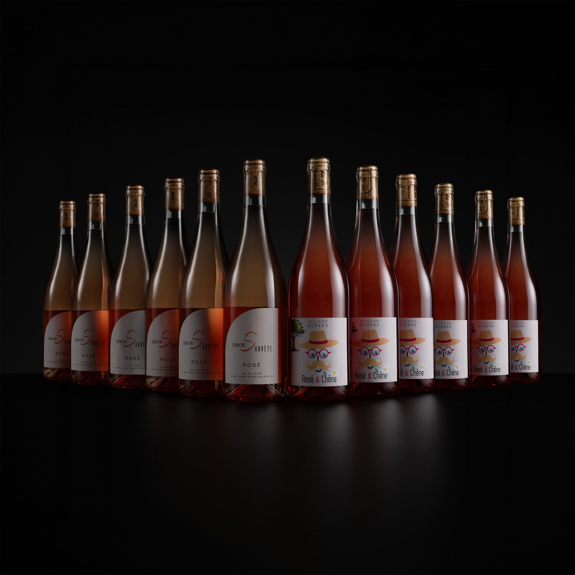 A row of ten glass rosé wine bottles with gold caps and white labels, arranged in a semi-circle on a black reflective surface against a black background. The labels feature the brand name 'Saint-Simon' and the cuvé 'Les Ducs'.