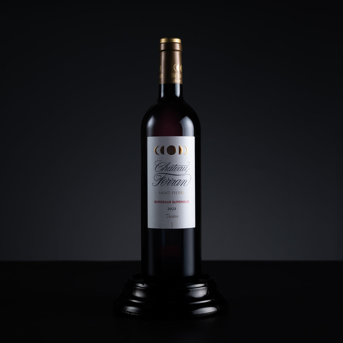 A bottle of Chateau Ferraro Bordeaux Superieur 2015 red wine, presented on a black wooden pedestal against a dark studio background.