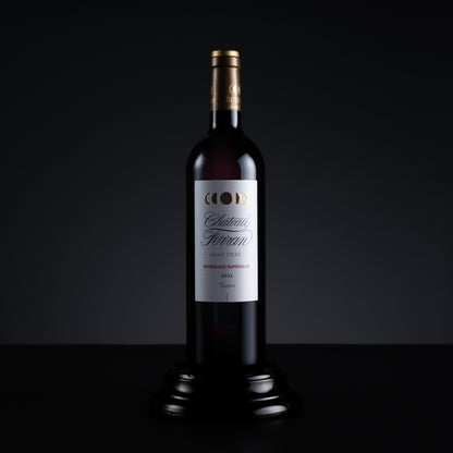 A bottle of Chateau Ferraro Bordeaux Superieur 2015 red wine, presented on a black wooden pedestal against a dark studio background.