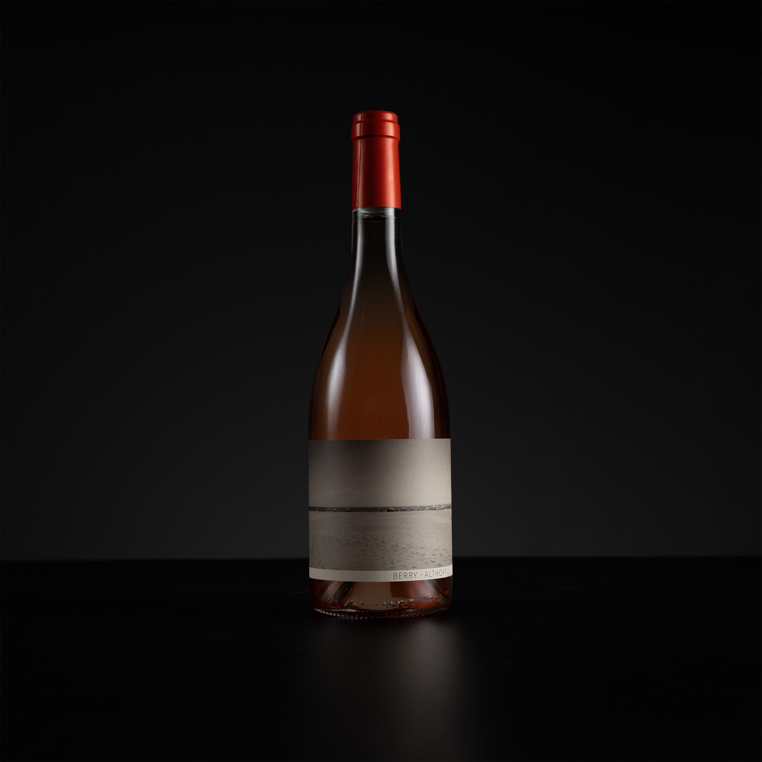 A single wine bottle with a red foil capsule and a blank beige label, standing on a dark reflective surface against a black background.