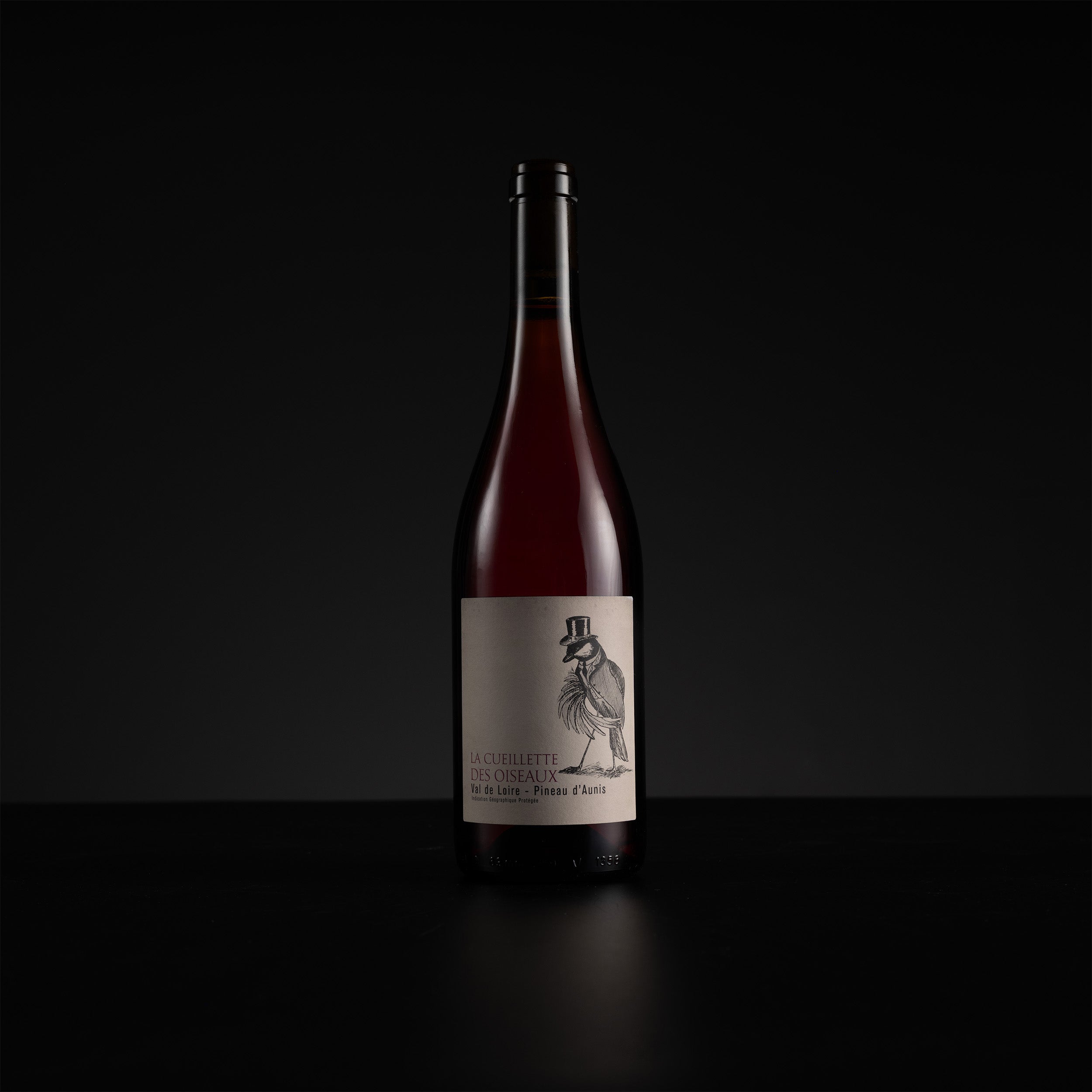 A single bottle of red wine with a cream-colored label featuring a black illustration of a rooster, set against a solid black background.
