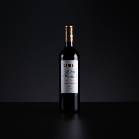 A single bottle of Château Ferran Red Wine (Cabernet Sauvignon) standing upright on a dark reflective surface against a solid black background.