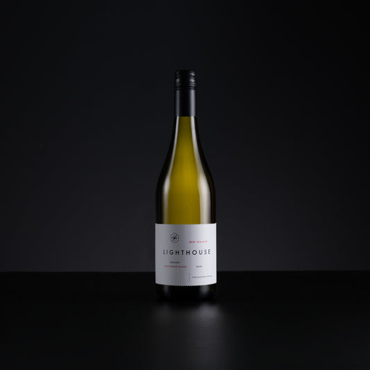 A single bottle of Lighthouse New Zealand Sauvignon Blanc wine, standing upright on a dark reflective surface against a solid black background.