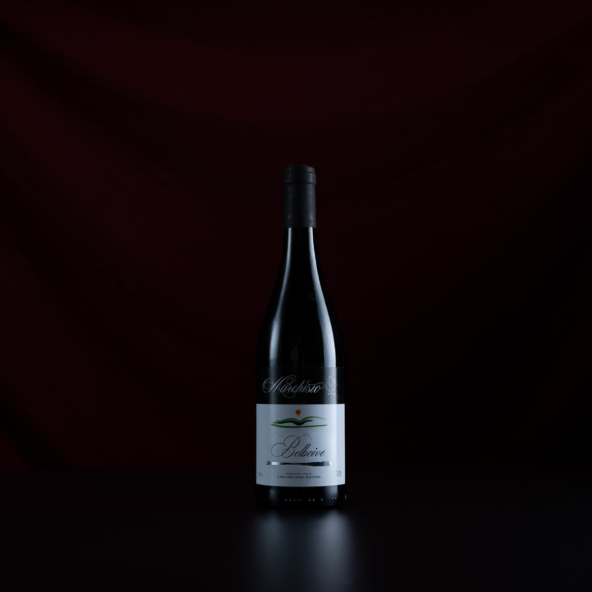 A single dark wine bottle with a white label stands centered against a very dark red and black draped background. The label text appears to read 'Mondial' and 'Pleure'.