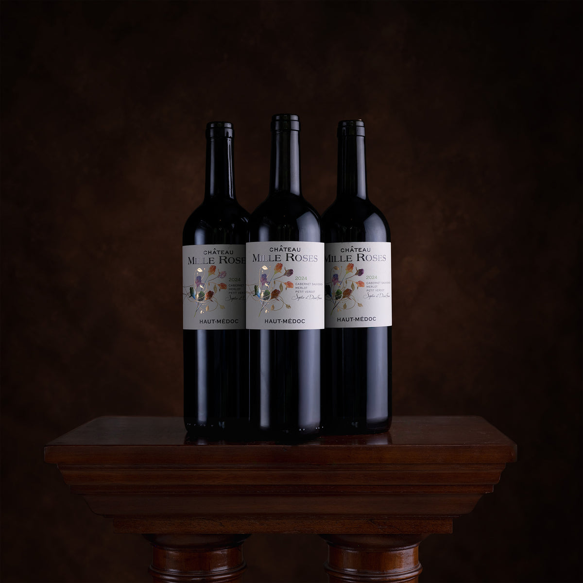 Three dark wine bottles with white labels reading Mille Rosé stand on a wooden pedestal against a dark brown studio background.