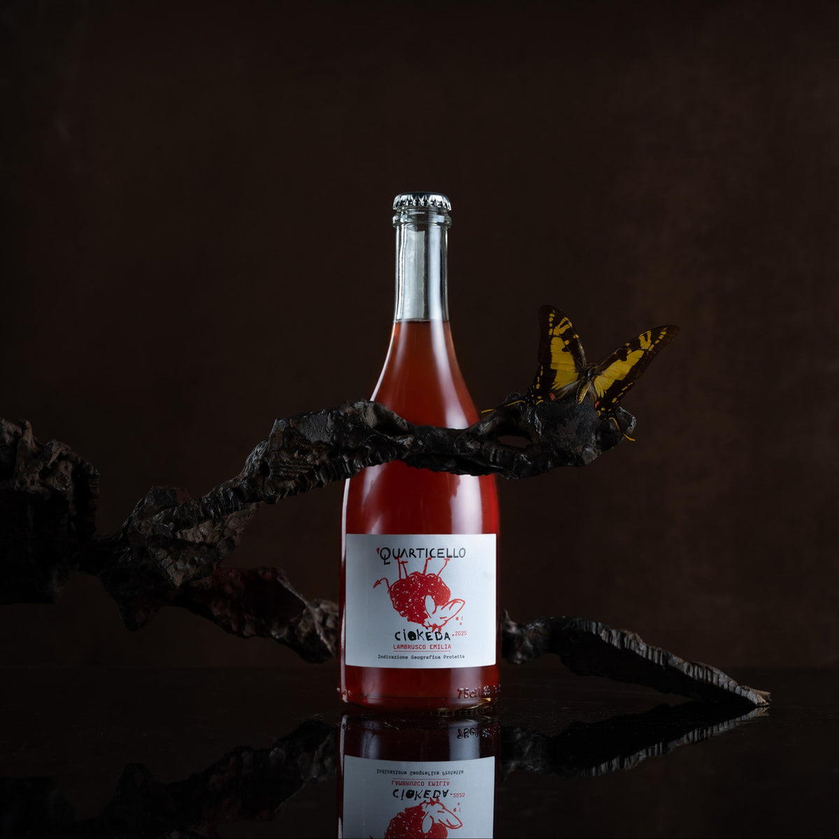 A bottle of Quartello Cintra rosé wine with a white label and red graphic, displayed on a dark reflective surface with a decorative branch and butterfly against a dark brown background.