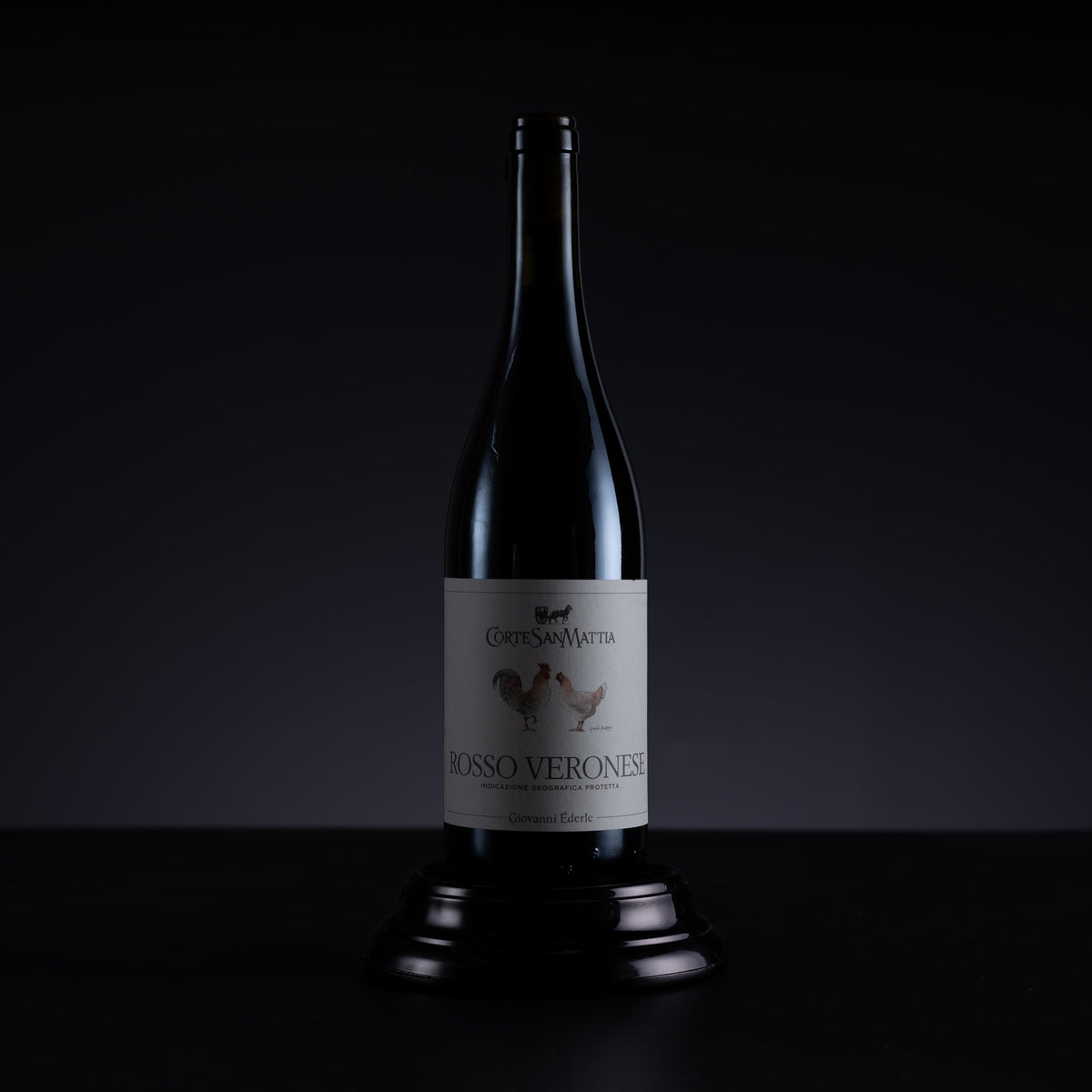 A dark glass bottle of wine with a cream-colored label reading 'Corte San Mattia Rosso Veronese', displayed on a dark pedestal against a black background.