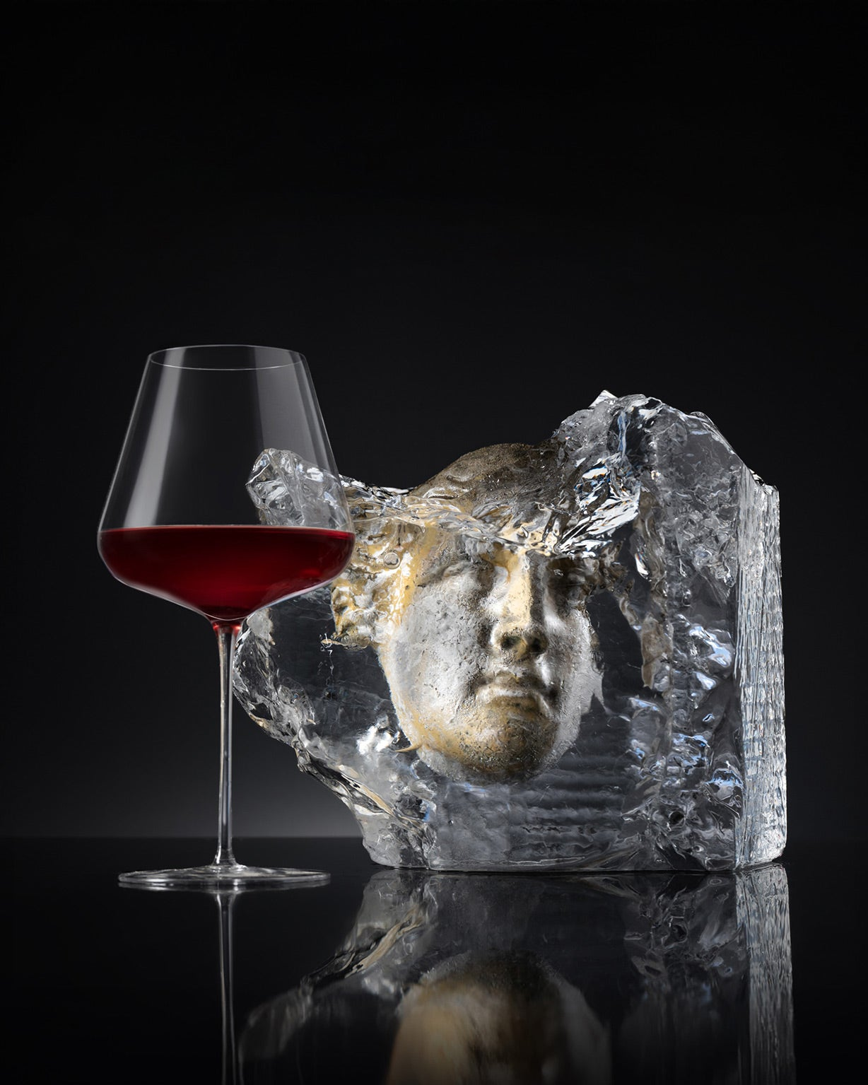 Glass of red wine next to a crystal sculpture on a black background