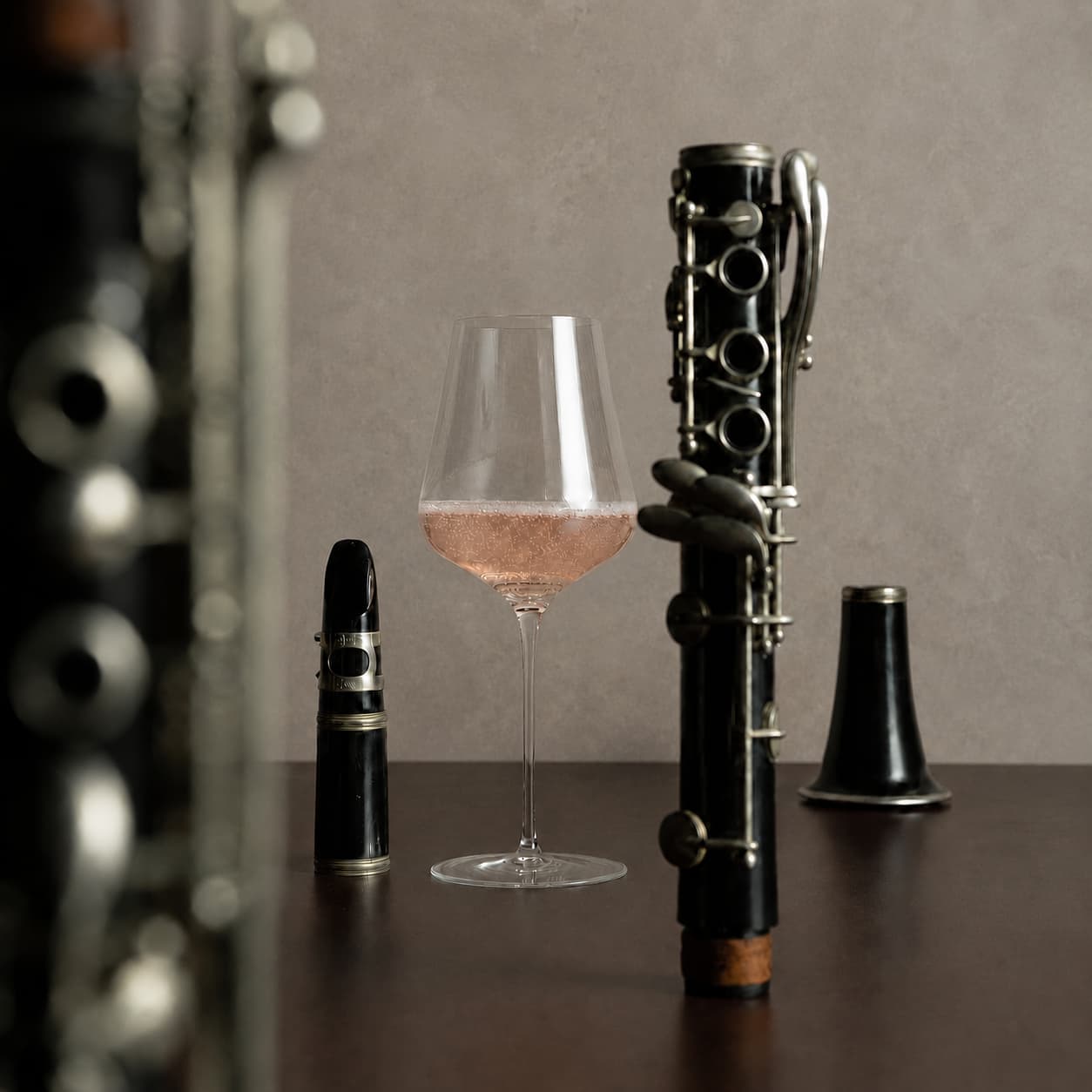 Clarinet parts and a glass of pink wine on a wooden surface with a gray background